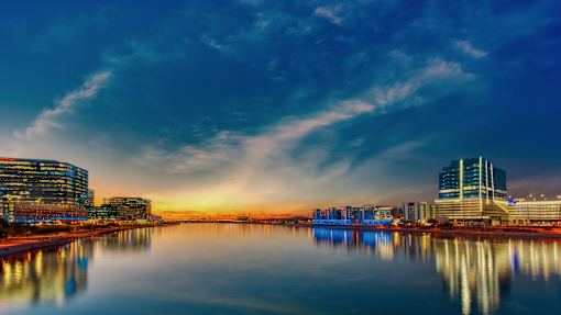 A cityscape at dusk with buildings reflecting in the water.