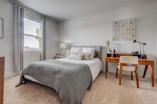 A bedroom with a bed, desk, chair, and window.
