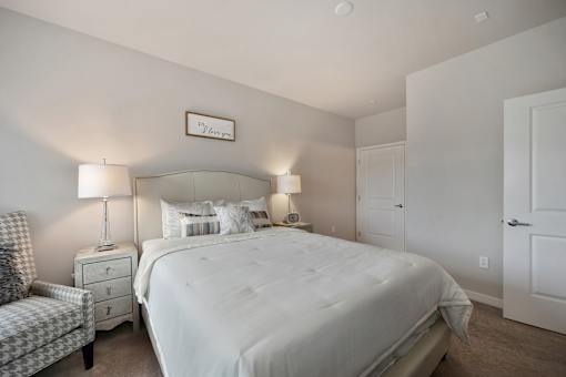 A bedroom with a large bed, a chair, and two lamps.