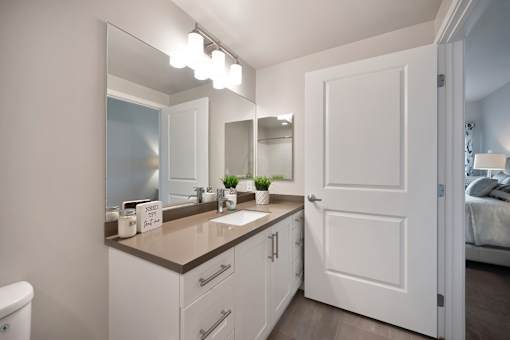 A bathroom with a white door and a mirror above the sink.