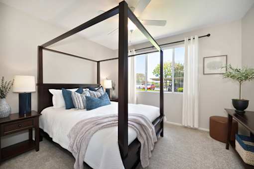 A bedroom with a four poster bed and a window with curtains.