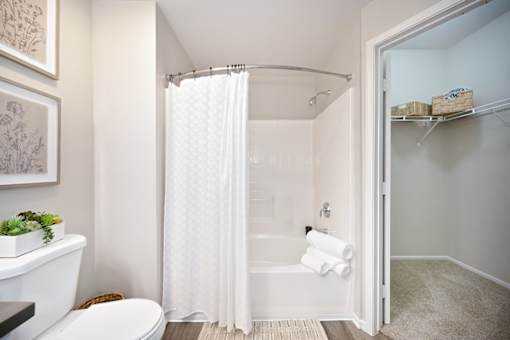 A white bathroom with a toilet, a bathtub, a shower curtain, and a plant.