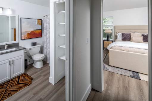 A white bathroom with a toilet, sink, and a bedroom with a bed.