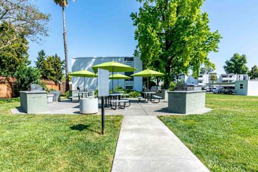 A sunny day at a park with picnic tables and green umbrellas.