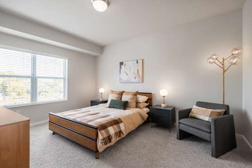 A bedroom with a large bed, a chair, and a painting on the wall.