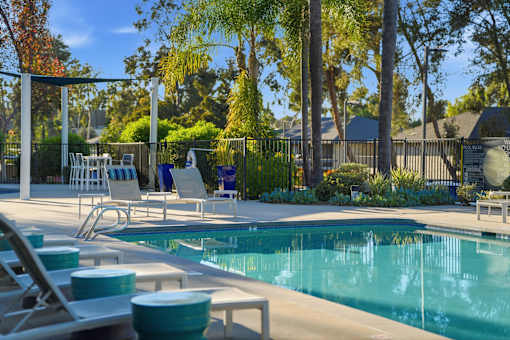 A pool surrounded by trees and chairs.