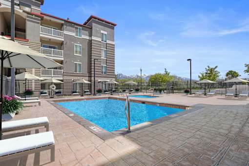 A large swimming pool surrounded by a tiled patio and apartment buildings.