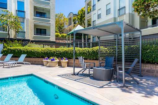A pool with a hot tub and chairs under a canopy.