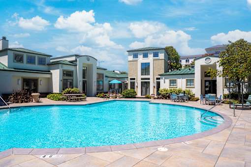 A swimming pool surrounded by a patio with chairs and a building in the background.