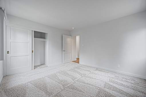 A room with white walls and a carpeted floor with a door on the left at Hillsdale Garden Apartments, CA 94403