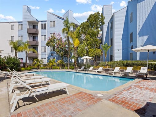 a swimming pool with chaise lounge chairs and umbrellas in front of an apartment building at Enclave, California