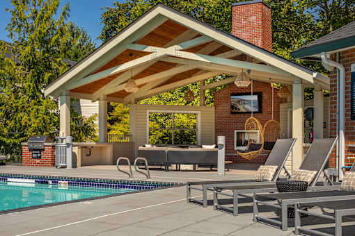 A poolside patio with a covered seating area and a brick chimney.