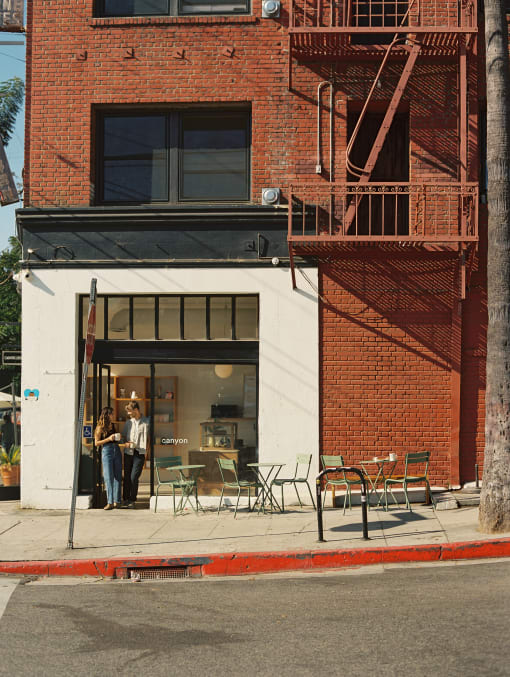two women stand in the doorway of a restaurant on a city street at Del Mor Apartments, Los Angeles, California
