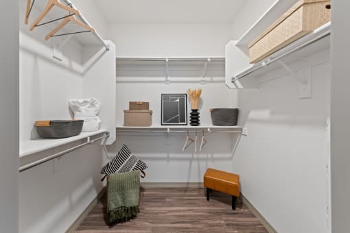 a walk in closet with shelves and baskets and a wooden floor and a white wall