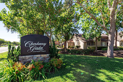 A sign for Chardonnay Garden Apartment Homes is surrounded by greenery.