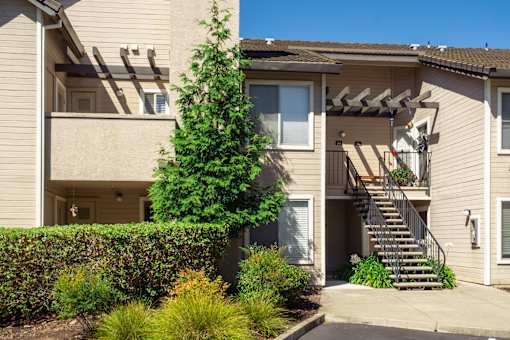 A beige two-story apartment building with a tree in front.