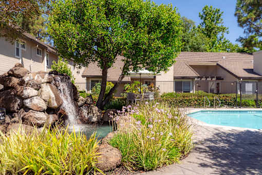 A pool with a waterfall and a tree in the middle of a garden.