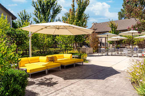 A yellow couch is sitting under a white umbrella in a courtyard.