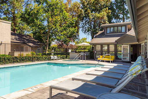 A pool with sun loungers and a house in the background.