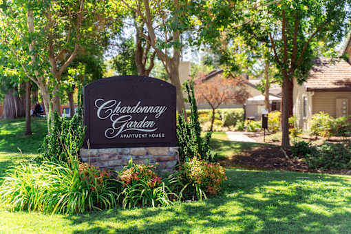 A sign for Chardonnay Garden Apartment Homes is surrounded by plants and trees.