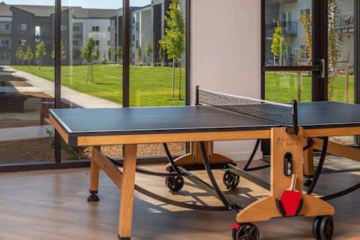 A ping pong table with a wooden base and a black top is in the foreground with a view of a grassy area and buildings in the background at The Arvon, Vancouver, WA 98662