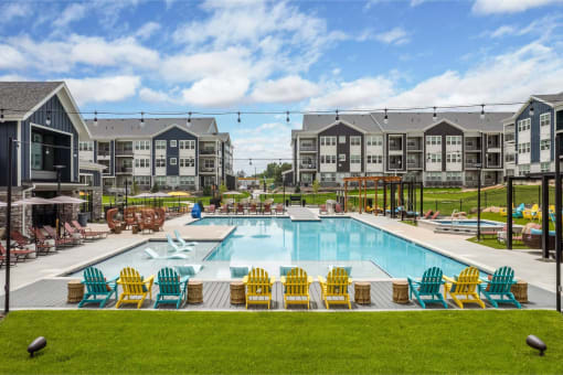 an outdoor pool with yellow and blue chairs around it and apartments in the background