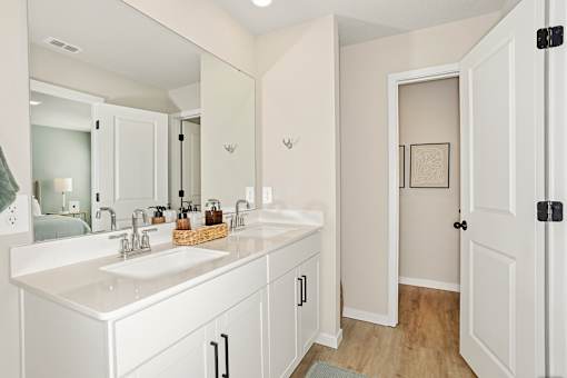 A white bathroom with a double sink and a mirror.