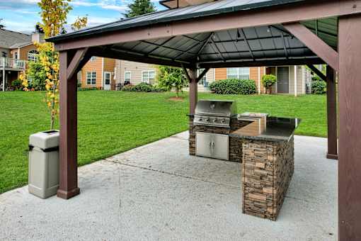 A covered patio with a grill and a trash can.
