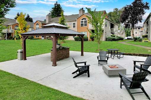 A gazebo is surrounded by black chairs and a fire pit in a grassy area.