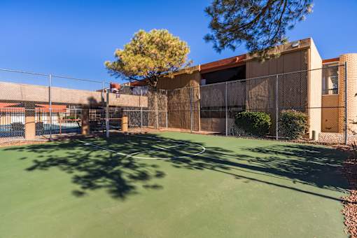 A tennis court is surrounded by a chain link fence and a building.
