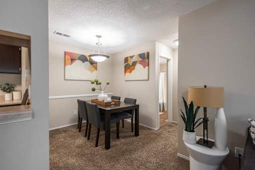 A dining room with a table set for two and a lamp on a side table.