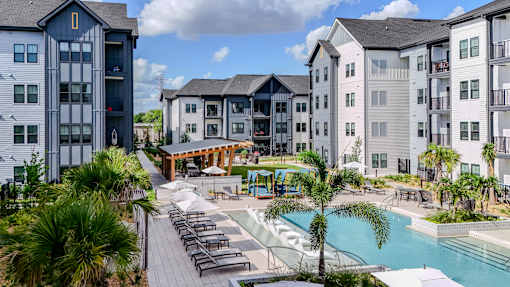 A pool area with a slide and sun loungers in front of apartment buildings.