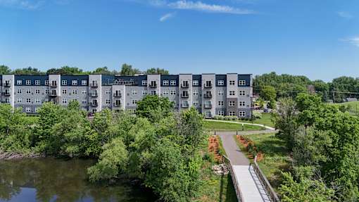 A row of modern apartment buildings are surrounded by trees and a small lake.