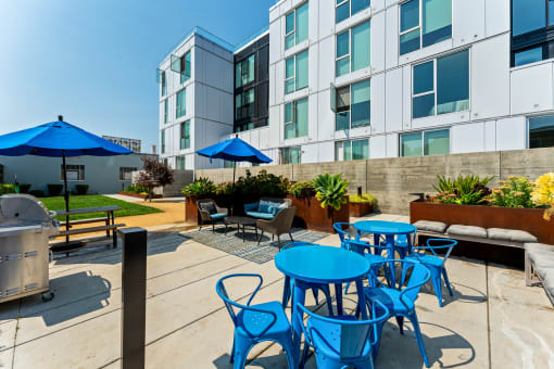an outdoor patio with blue tables and chairs and an apartment building in the background