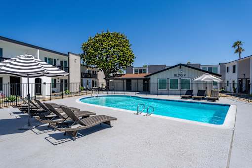 A pool with sun loungers and umbrellas in front of a building with BLDG 9 on it.