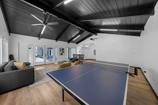 A ping pong table is in the middle of a room with a grey couch and a wooden floor.