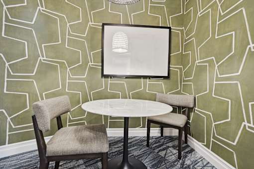 A white table with two chairs in front of a green wall with a picture frame.