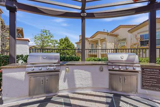 A barbecue grill is located under a pergola with a plaque beside it.