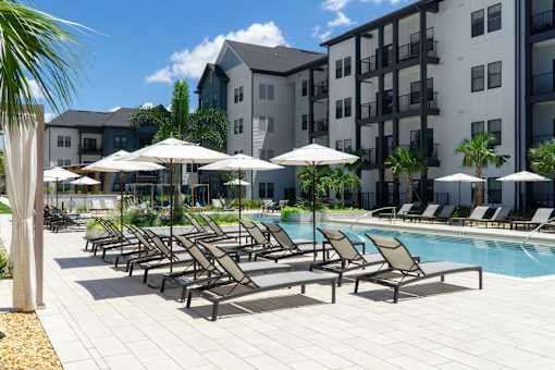 A pool area with sun loungers and umbrellas in front of apartment buildings.