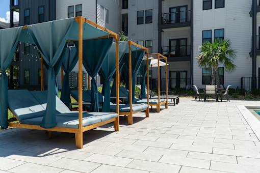 A row of wooden daybeds with green canopies are lined up on a patio.