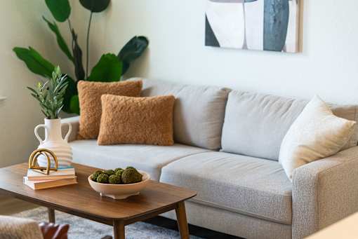 A living room with a grey couch, a wooden table with a bowl of green fruit and a stack of books on it.