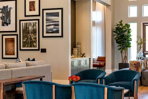 A living room with a grey couch, blue chairs and pictures on the wall.