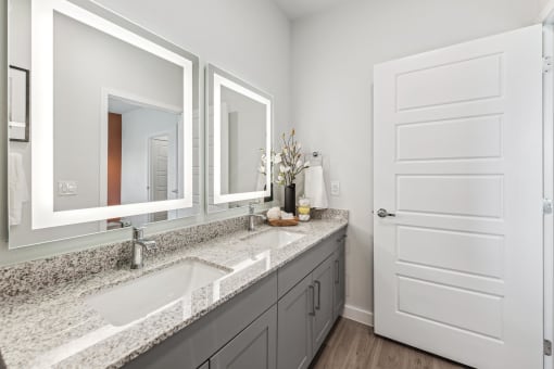 bathroom with back lit mirrors and granite countertops