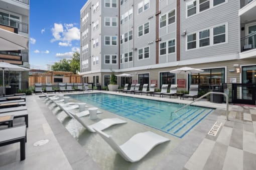 a swimming pool with lounge chairs in front of an apartment building