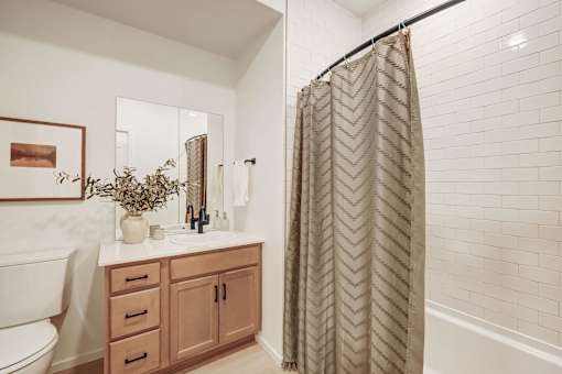 A bathroom with a white toilet, a sink with a mirror, a plant, and a shower curtain.