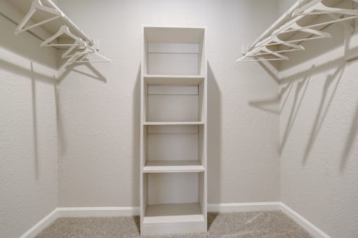 a walk in closet in a bedroom with white shelves and white walls