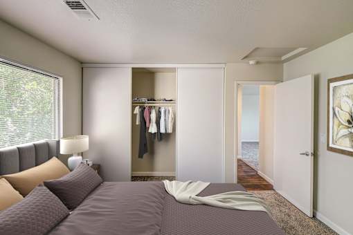 A bedroom with a large bed and a closet with clothes hanging.