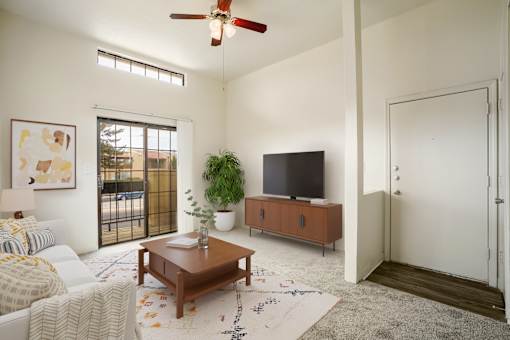 A living room with a white couch, a wooden coffee table, a flat screen TV, and a ceiling fan.