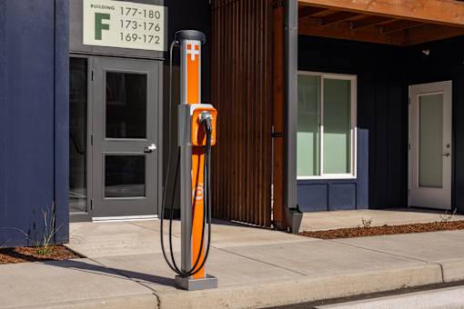 A tall orange pole with a cross on it stands in front of a building.