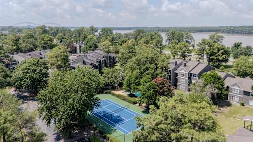 A tennis court is surrounded by trees and houses.